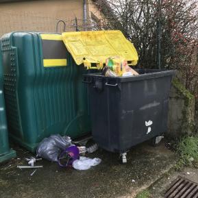 Bac jaune ouvert et sac de déchets posé au sol.